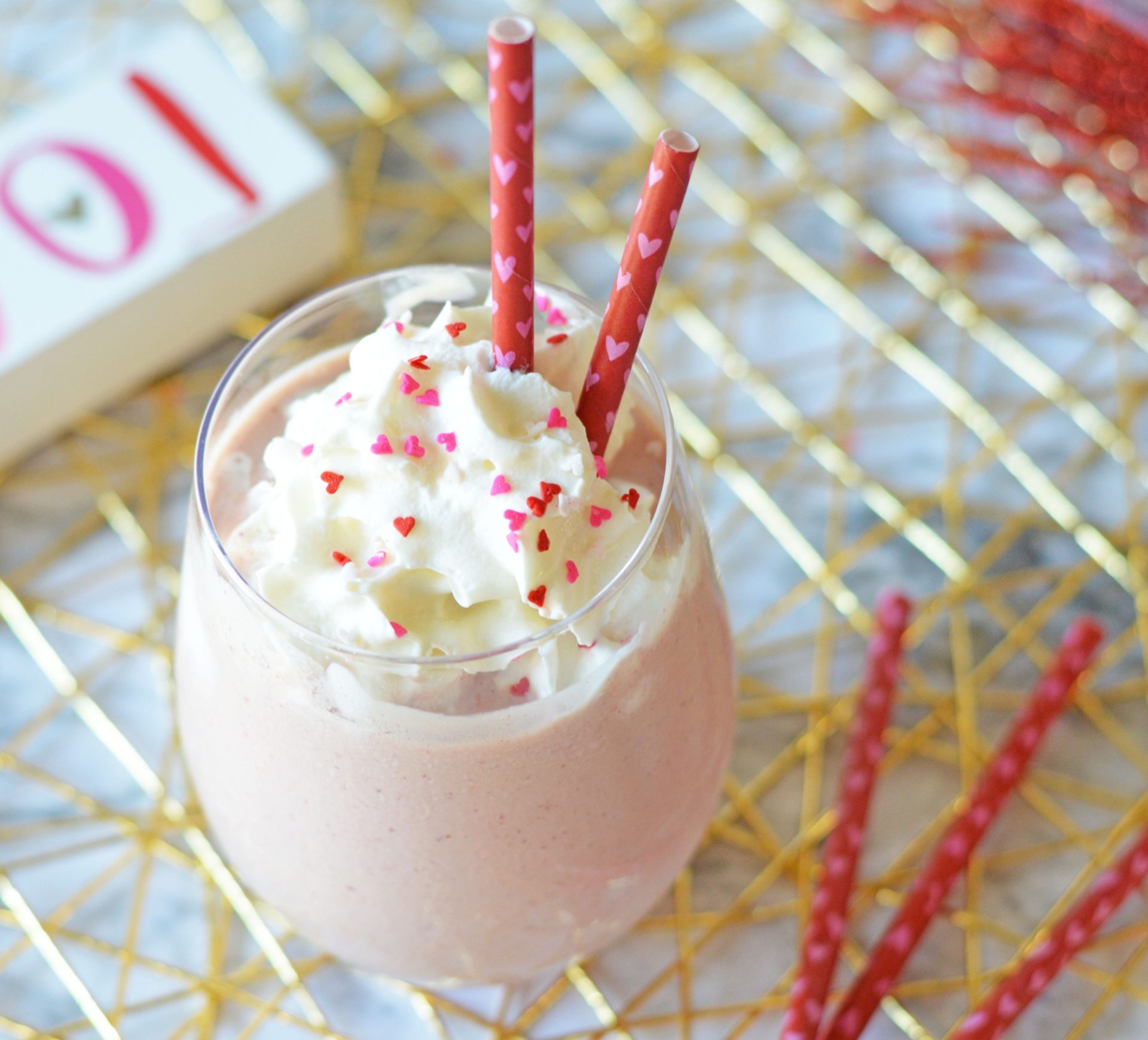A Bailey's pink mudslide cocktail in a tall glass, garnished with whipped cream, springles and straws.