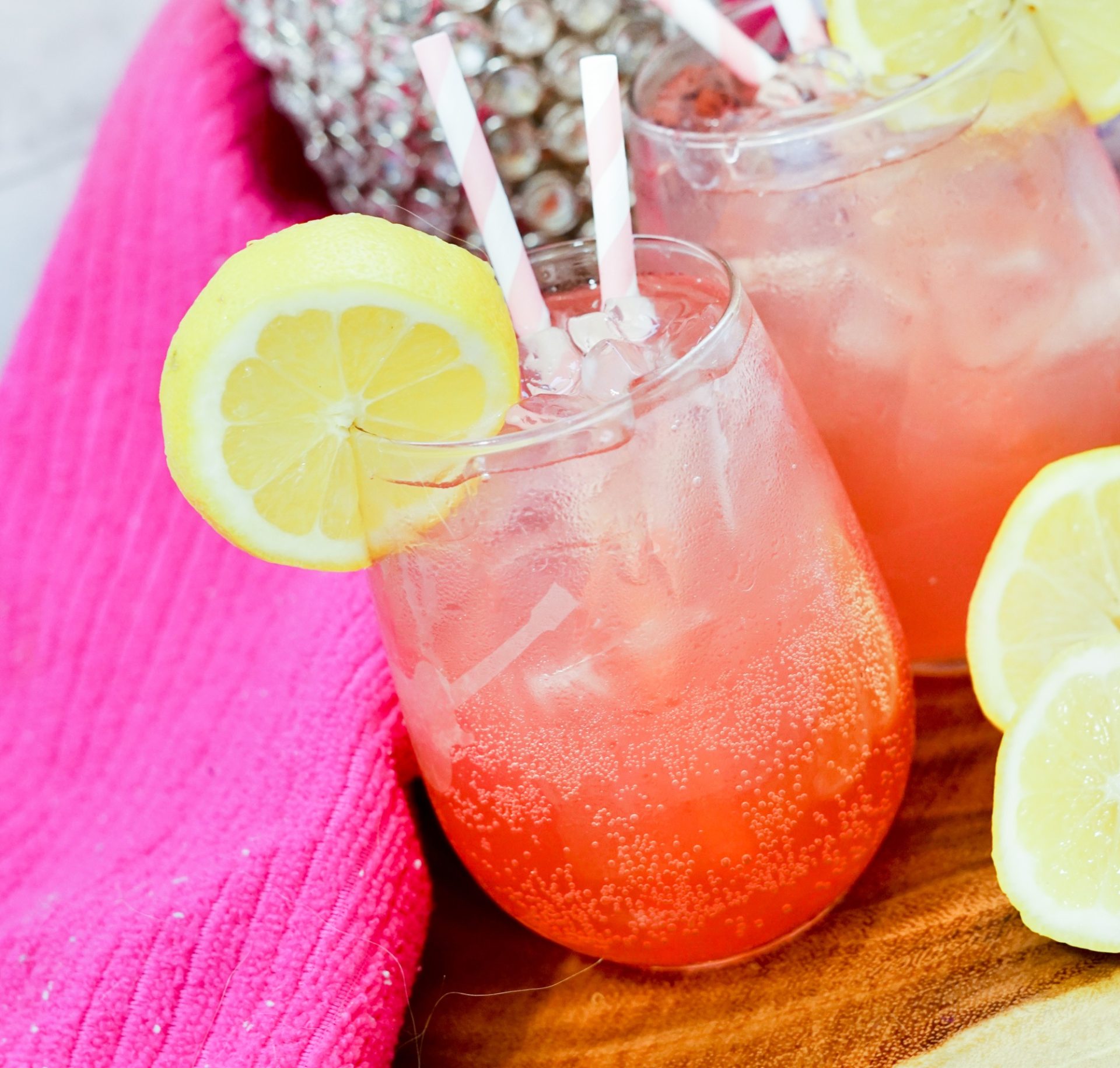 Barbie girl Galentine's day cocktail in a glass over ice. Garnished with lemon slice and pink straws.