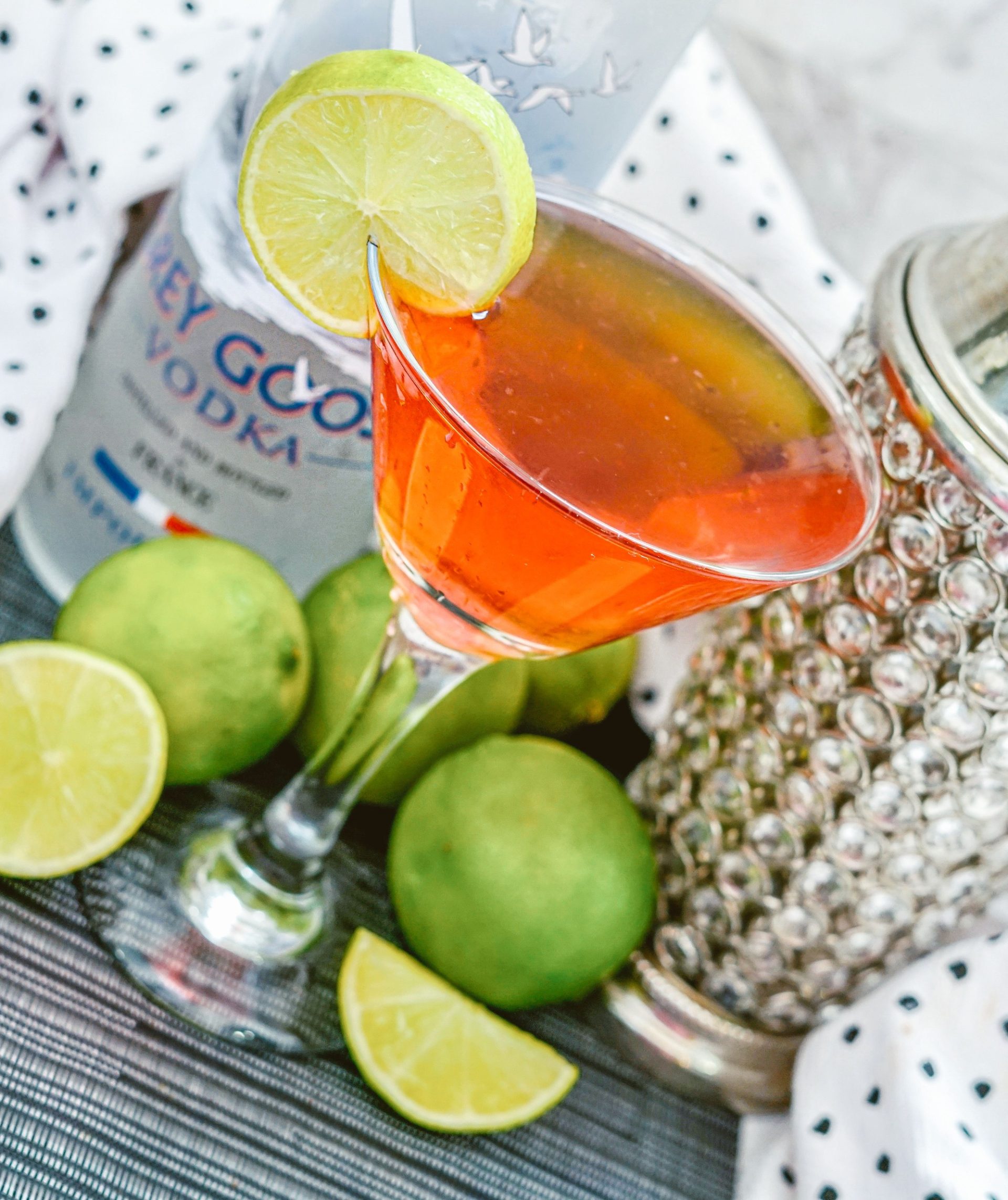 Galentine's Cosmo cocktail in a martini glass on a table with cocktail shaker, vodka and limes.