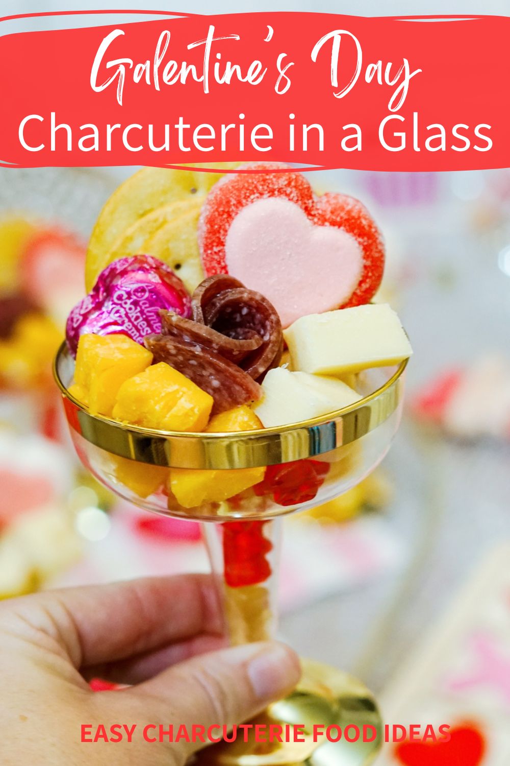 Galentine's Day charcuterie in a glass being held by a woman. Glass is filled with meat, cheese, crackers and chocolate.