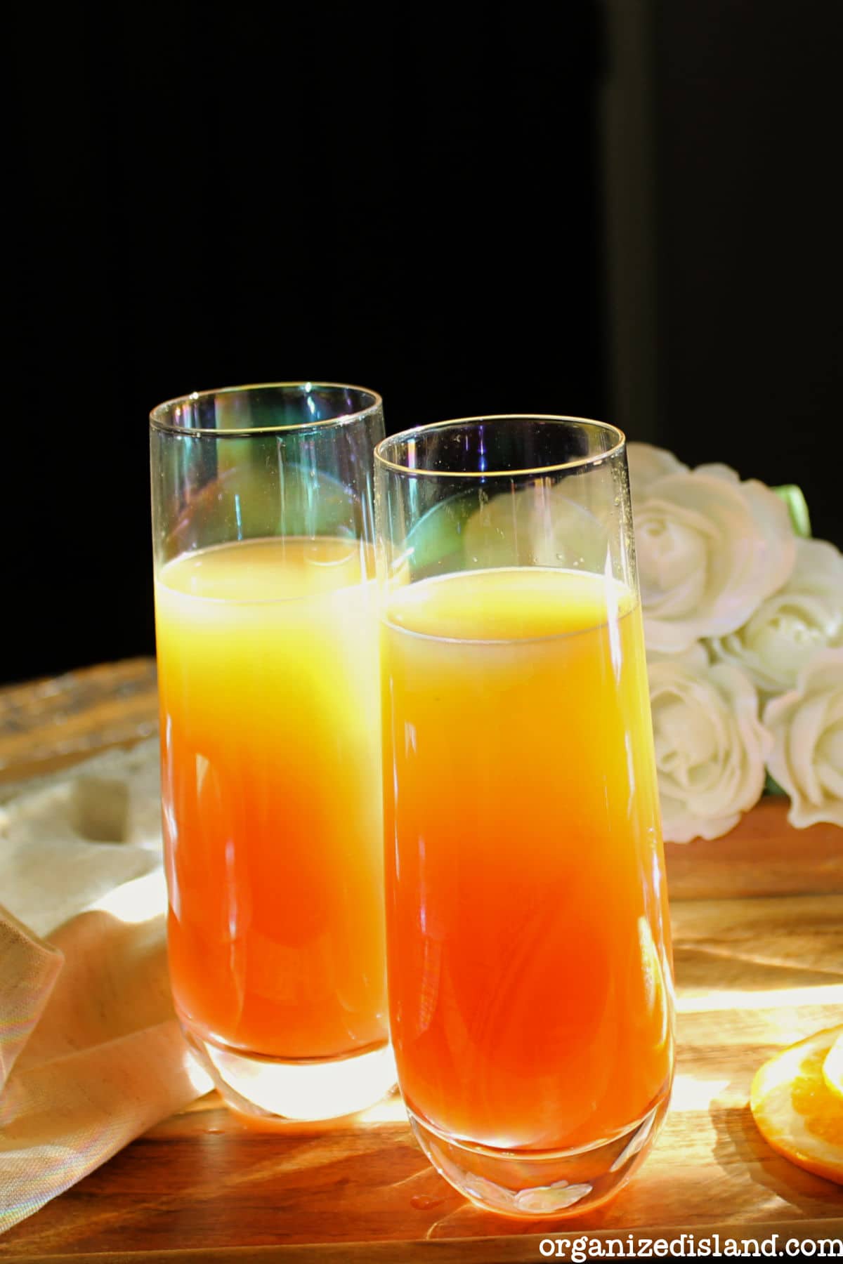 Two tequila sunrise mimosas in flutes sit on a table.