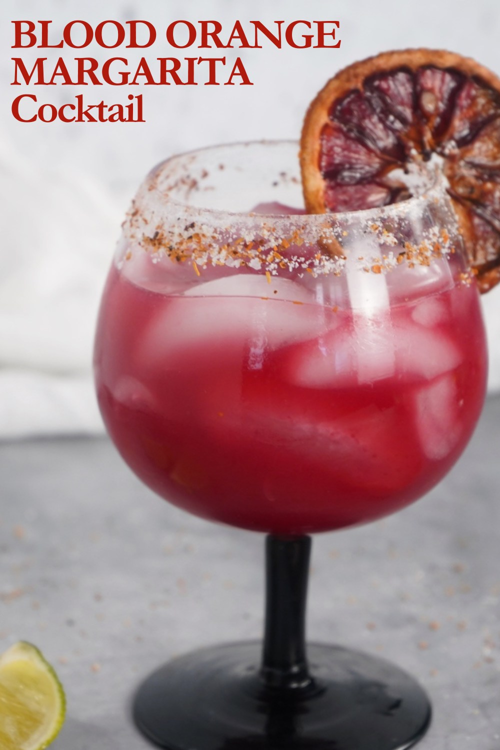 Blood orange margarita in a glass with ice and a Tajin rim.