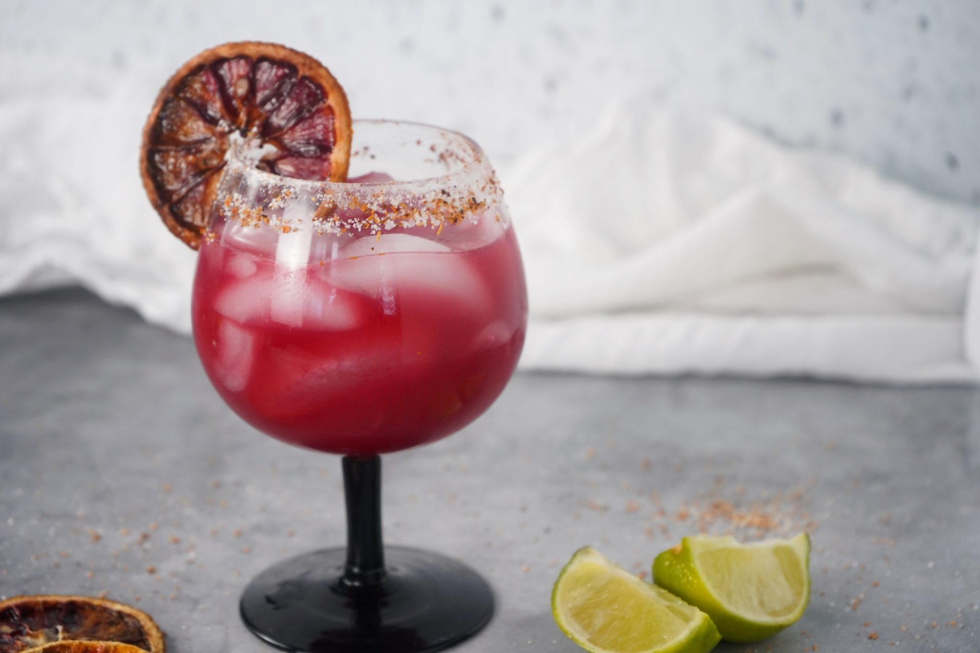 Blood orange margarita in a tajin rimmed glass with a slice of dried blood orange garnish.