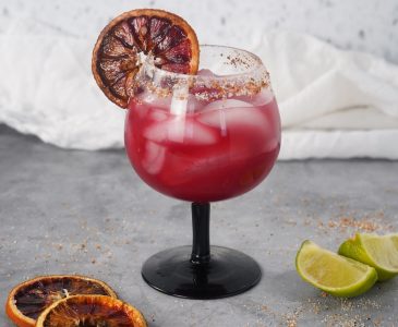 Blood orange margarita cocktail in a glass over ice with blood orange slice garnish.