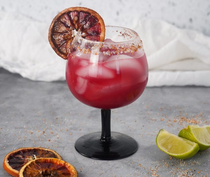 Blood orange margarita cocktail in a glass over ice with blood orange slice garnish.